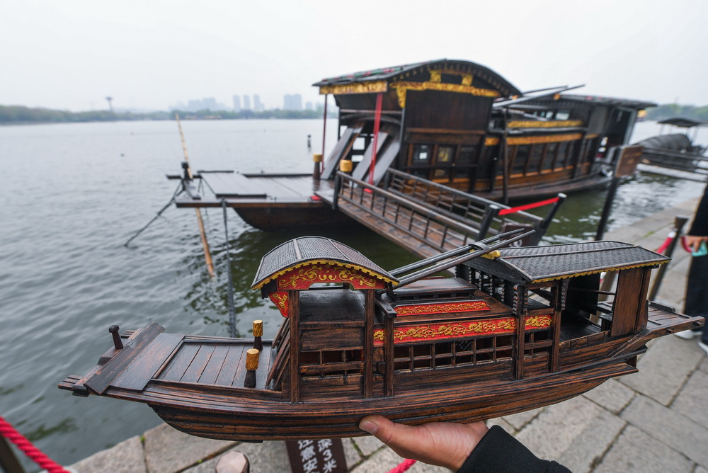 4月13日，韩鸣华拿着自己制作的红船模型站在嘉兴南湖湖心岛的红船边。