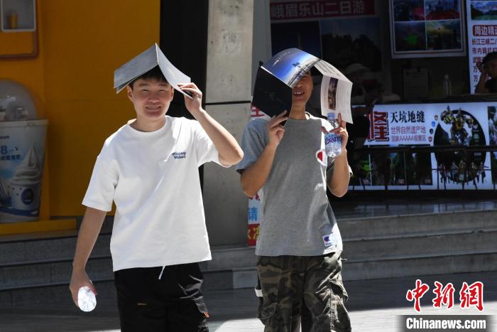 重庆街头，外出的市民用纸板遮头防晒。　周毅 摄
